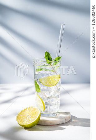 Mojito cocktail in a glass with lime, mint, ice and tube on a white blue background with shadows. 126082460