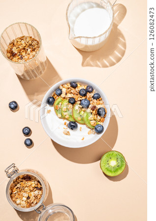 Natural yogurt with granola, kiwi and blueberries in a bowl on a beige background. Natural yogurt with granola, kiwi and blueberries in a bowl on a beige background. 126082473