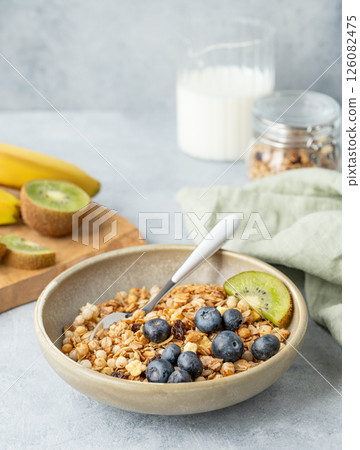 Homemade baked granola or muesli in a bowl with kiwi and blueberries on a light background 126082475