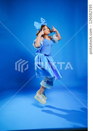 Cute teenage girl in blue doll dress with big blue bow jumping. 126082595