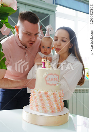 Mom and dad hold little daughter by the birthday cake. Mom and dad hold little daughter by the birthday cake. 126082598