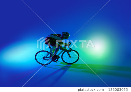 Top view of man, professional cyclist in motion, riding bicycle, training against blue background with green neon light Top view of man, professional cyclist in motion, riding bicycle, training against blue background with green neon light 126083053