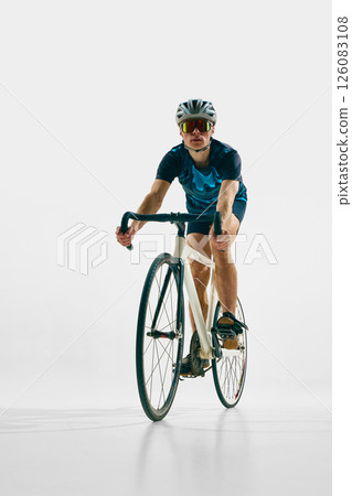 Full-length front view image of young man in full gear, cyclist in helmet and goggle riding bicycle isolated on white background. 126083108