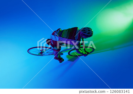 Top view of professional male cyclist in motion, training against blue studio background with green neon light. 126083141
