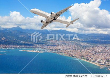 White passenger airplane flying over coastal city, mountains and blue sea 126083703