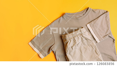 Set of light gray children's clothes T-shirt with trousers. Fashion kids outfit for summer and spring. Total grey look on yellow background. Flat lay, top view Set of light gray children's clothes T-shirt with trousers. Fashion kids outfit for summer and spring. Total grey look on yellow background. Flat lay, top view 126083856