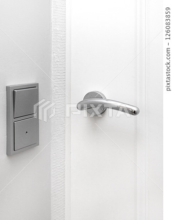 Modern chrome door handle and light switch on white wall 126083859