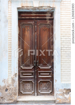 Weathered carved wooden double door in crumbling facade 126083993