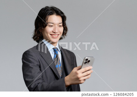 A young businessman smiling while looking at his smartphone 126084205