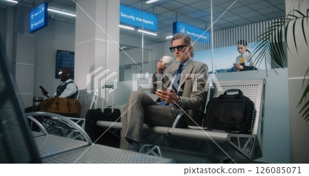 Airport Terminal: Successful Man Sitting in Departure Lounge, Using Cellphone and Drinking Coffee 126085071