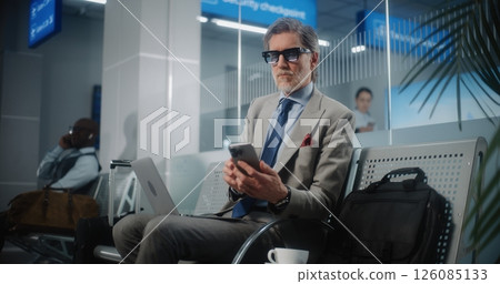 Airport Terminal: Successful Entrepreneur with Laptop Sitting in Departure Lounge, Using Phone Airport Terminal: Successful Entrepreneur with Laptop Sitting in Departure Lounge, Using Phone 126085133