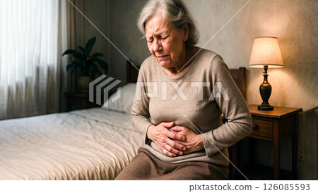 Elderly woman experiencing stomach pain in dimly lit bedroom setting with emotional expression 126085593