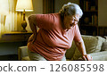 Elderly woman experiencing back pain while rising from sofa in living room 126085598