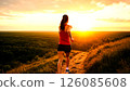 Woman jogging on scenic hilltop trail at breathtaking sunset overlooking vast forest 126085608
