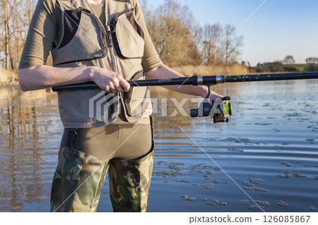 Fisherwoman wearing fishing waders holding fishing rod in river Fisherwoman wearing fishing waders holding fishing rod in river 126085867