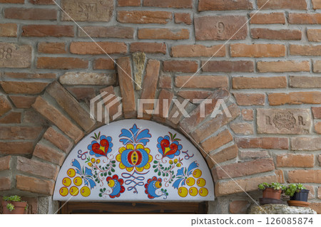 Colorful hungarian kalocsai embroidery decorating a brick arch above a window 126085874