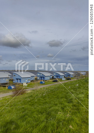 Row of modern blue bungalows facing the river under cloudy sky 126085948