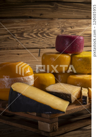 Various cheese wheels and slices resting on wooden pallet against rustic background Various cheese wheels and slices resting on wooden pallet against rustic background 126085955