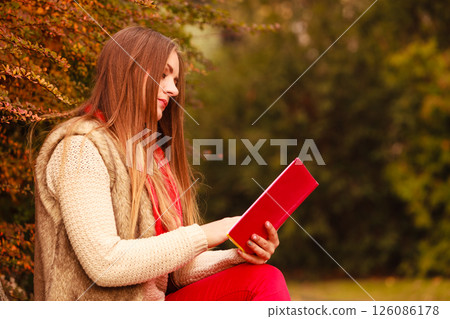 Woman relaxing in autumnal park reading book Woman relaxing in autumnal park reading book 126086178