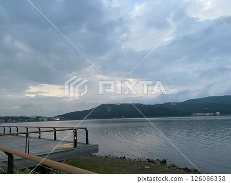 Lakeside promenade at dusk, with lit-up mountains on the opposite shore Lakeside promenade at dusk, with lit-up mountains on the opposite shore 126086358