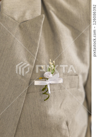 Groom wearing light gray suit with white rose boutonniere and white ribbon Groom wearing light gray suit with white rose boutonniere and white ribbon 126086392
