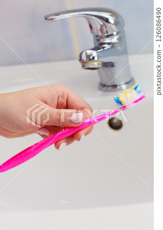 Hand holding toothbrush in bathroom 126086490