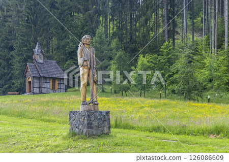 Wooden statue of a lumberjack standing in front of a small wooden church in the forest 126086609