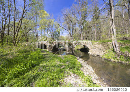Old stone bridge crossing Doubrava river near Zasmuky in Czechia surrounded by spring greenery 126086910