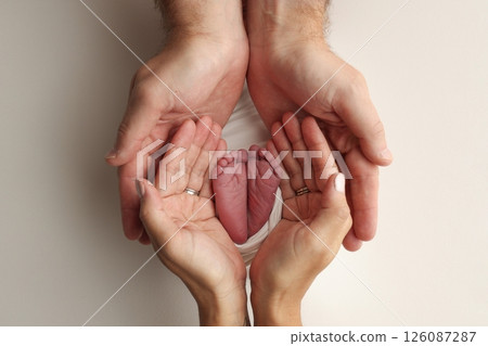 A father and mother hold the feet of a newborn child in a white blanket on a white background.. The feet of a newborn in the hands of parents. Photo of foot, heels and toes.The palms of the parents. 126087287