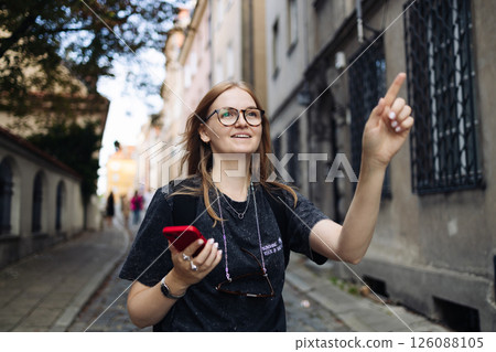 Smiling woman with smartphone pointing forward while exploring city Smiling woman with smartphone pointing forward while exploring city 126088105