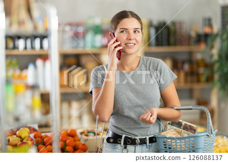 Female shopper talking on smartphone while shopping in grocery supermarket Female shopper talking on smartphone while shopping in grocery supermarket 126088137