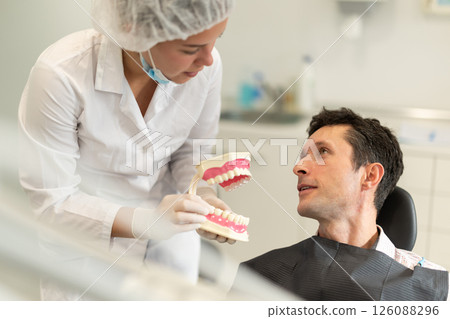 Young woman dentist communicates with male patient, shows model of jaws 126088296