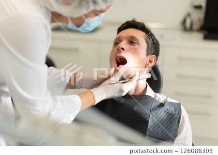 Girl doctor dentist in white coat examines oral cavity of man patient in dentistry. 126088303
