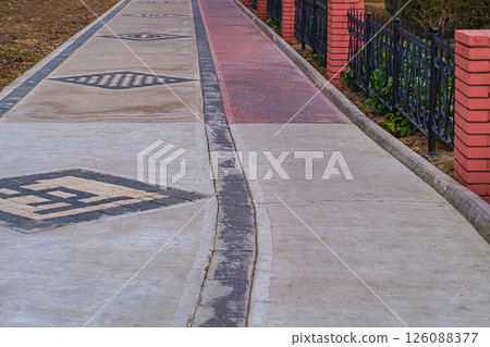 Urban pedestrian and bicycle street paths made of concrete, visually marked with color highlighting and built-in patterns with different paving stone symbols. Public places, landscaping elements 126088377