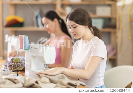 Two seamstresses working on sewing machines in sewing workshop Two seamstresses working on sewing machines in sewing workshop 126088444