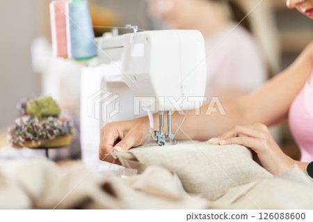Friendly middle aged woman tailor using sewing machine at workshop 126088600