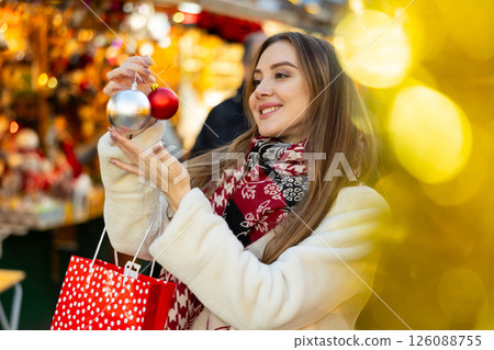 Woman at New Year fair and bustle is leisurely examining ball for decorating Christmas tree. 126088755
