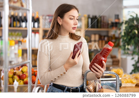 Girl customer holds bottle of tomato juice in hand, scans QR code on product label 126088799