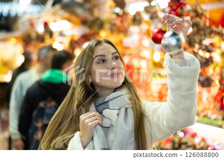 Woman at New Year fair and bustle is leisurely examining ball for decorating Christmas tree. 126088800