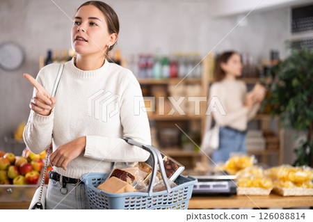 Portrait of girl shopper with a shopping cart choosing some products in supermarket 126088814