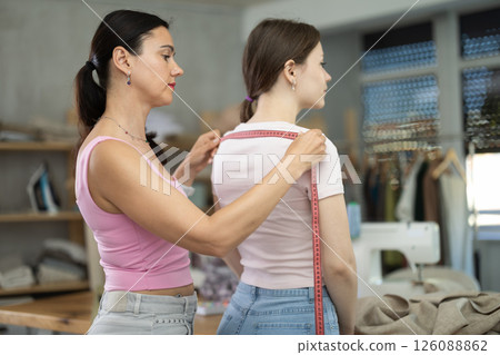 Woman tailor takes measurements from girl client Woman tailor takes measurements from girl client 126088862