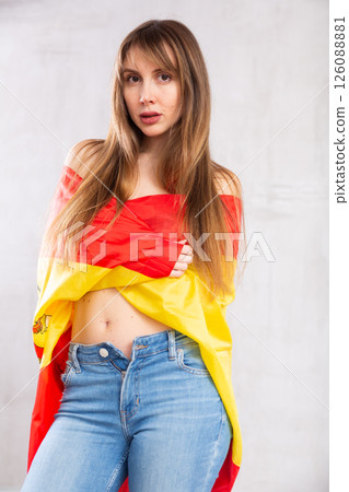 Flirting young woman posing with flag of Spain against gray wall 126088881