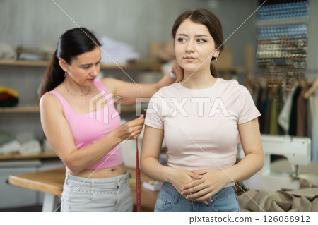 Woman tailor takes measurements from girl client Woman tailor takes measurements from girl client 126088912