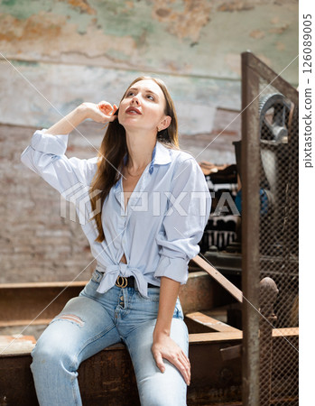 Young woman in jeans and tied shirt posing in destroyed plant 126089005