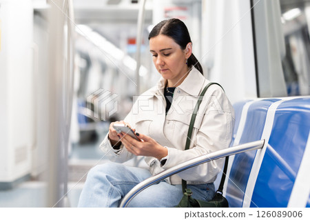 Girl in modern subway car scrolling smartphone 126089006