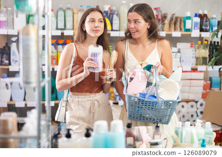 Two happy friends choosing different cosmetics, having full shopping cart with various purchases Two happy friends choosing different cosmetics, having full shopping cart with various purchases 126089079