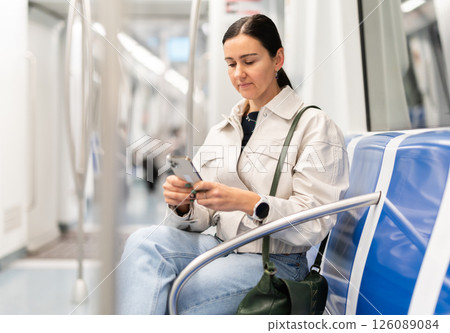 European woman sitting on seat in subway train and using smartphone European woman sitting on seat in subway train and using smartphone 126089084