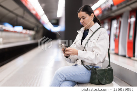 Girl with phone is sitting on metro platform station, scrolling though internet 126089095