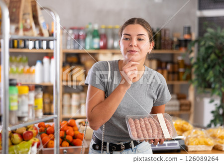 Girl shopping at shop - choosing raw sausages in grocery section Girl shopping at shop - choosing raw sausages in grocery section 126089264