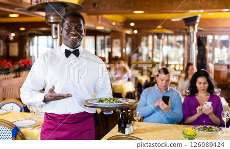 Positive African-american waiter with tray in restaurant 126089424